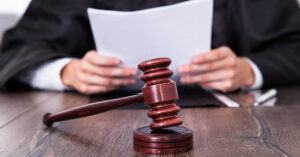 Judge with black cloak holding a small stack of papers with a gavel