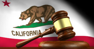 A wooden gavel sits on top of a table with the California state flag in the background