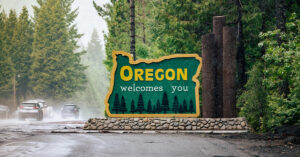 The state of Oregon road sign welcomes drivers on a rainy day with tall green pine trees in the background