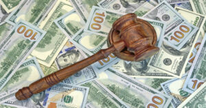 A wooden gavel sits on top of several 100-dollar bills.