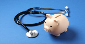 A piggy bank sits next to a stethoscope on a blue background