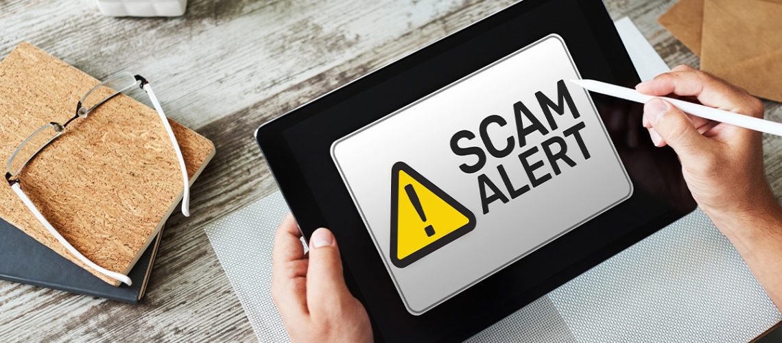 A person holding a digital tablet with a cautionary "Scam Alert" on the screen