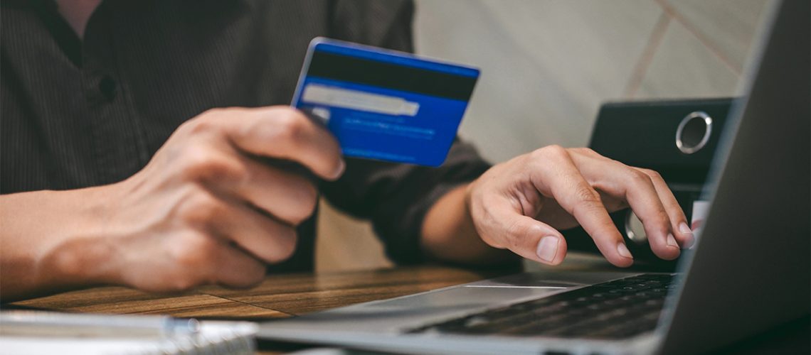 A person holding a credit card and entering information on their laptop