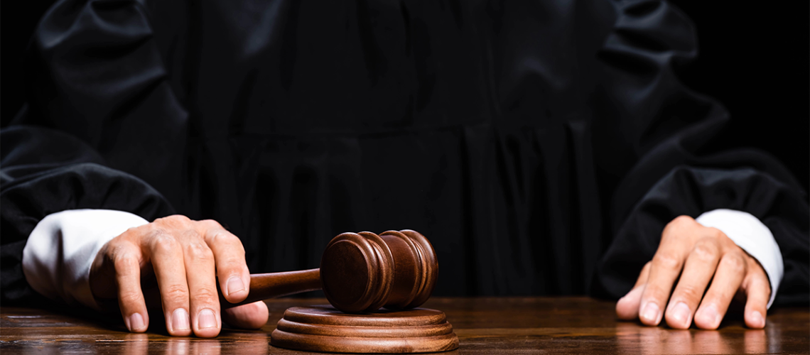 A judge sits at the table holding a wooden gavel