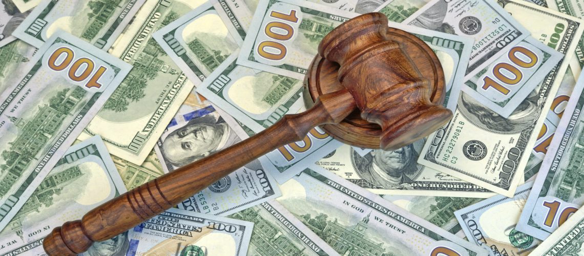 A wooden gavel sits on top of several 100-dollar bills.