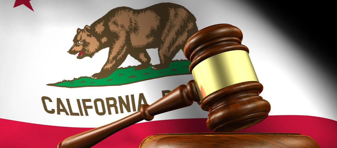 A wooden gavel sits on top of a table with the California state flag in the background