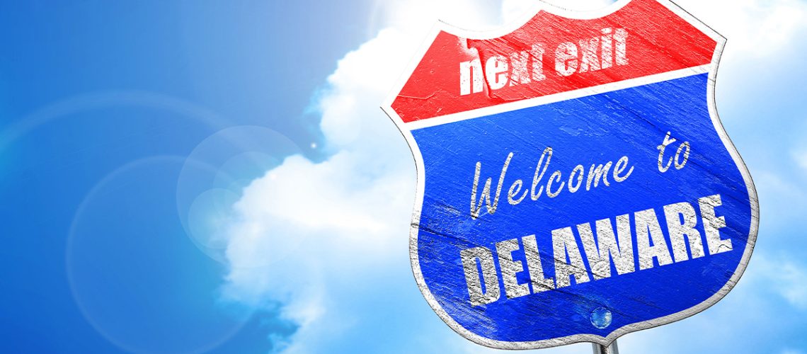A road sign says "next exit welcome to Delaware" in front of a partly cloudy blue sky