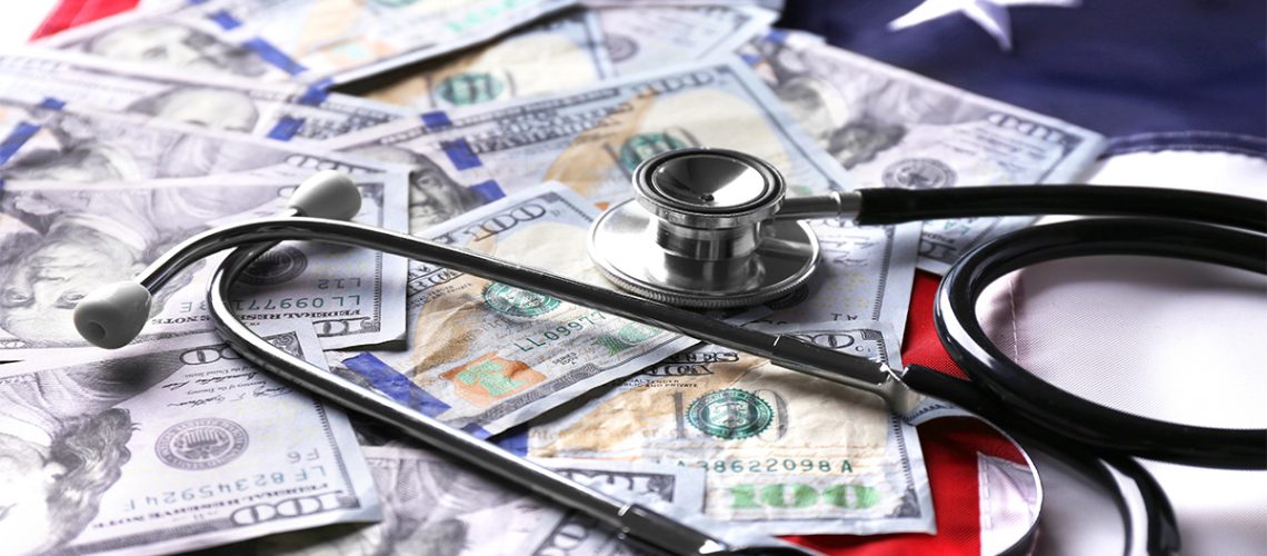 The American flag with scattered money bills and a stethoscope on top of it