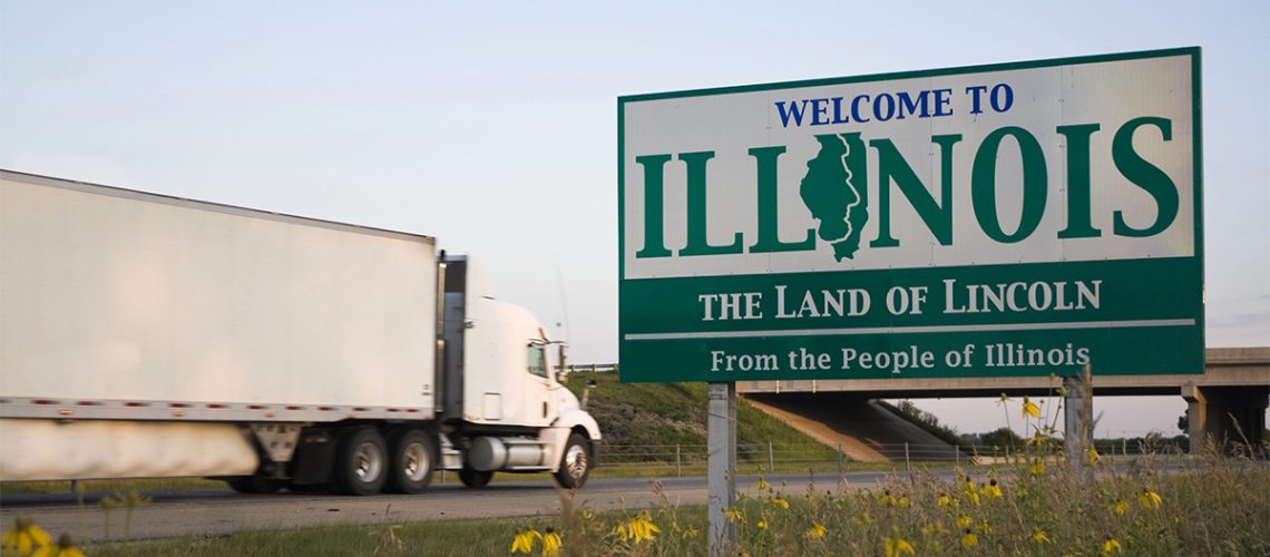 A white semi truck drives on a highway with the "Welcome to Illinois" road sign in the foreground.