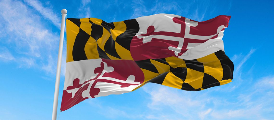 The Maryland flag attached to a flagpole waves in the wind with a partly cloudy sky in the background
