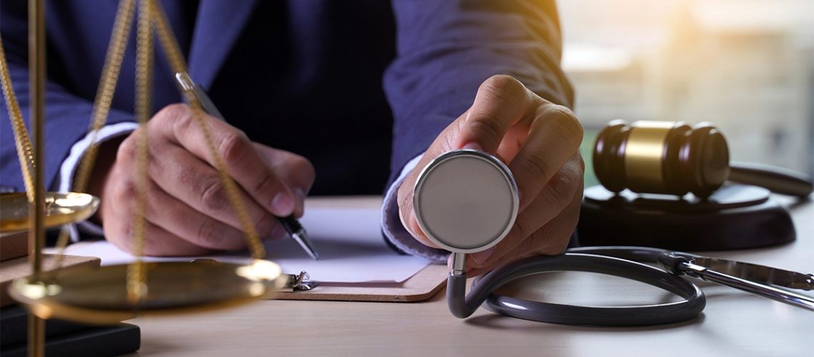 A person in an office holding up a stethoscope with a gavel on the table