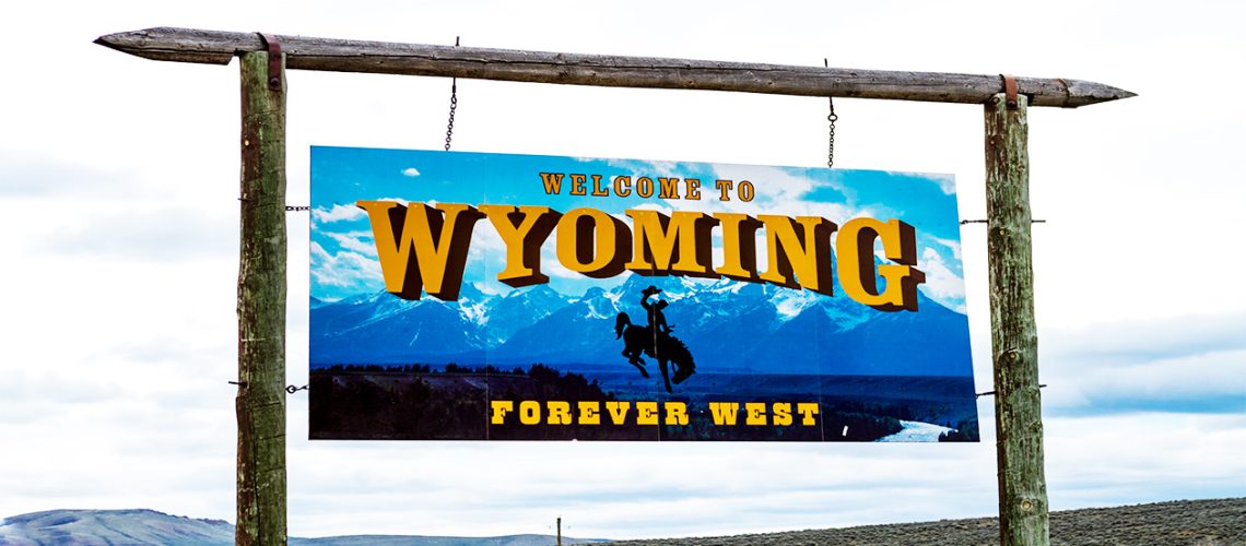 A sign that says "Welcome to Wyoming" and "Forever West" overlooks a landscape and cloudy skies.